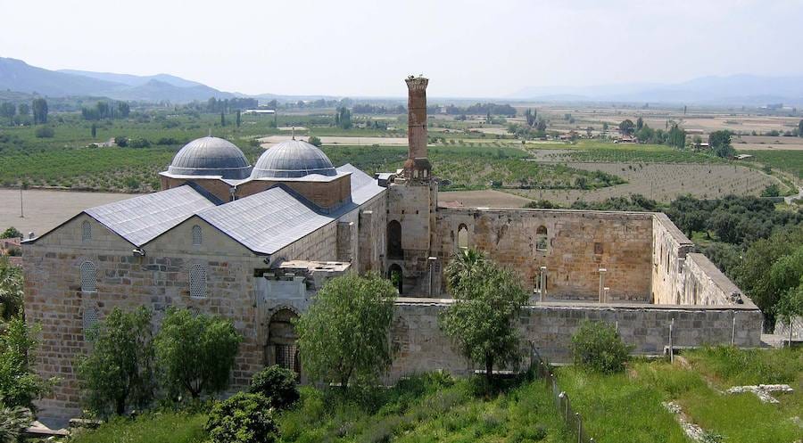 La mezquita de İsa Bey de Selçuk vista desde la colina, con sus dos cúpulas, el patio en ruinas y un nido de cigüeña sobre el alminar truncado