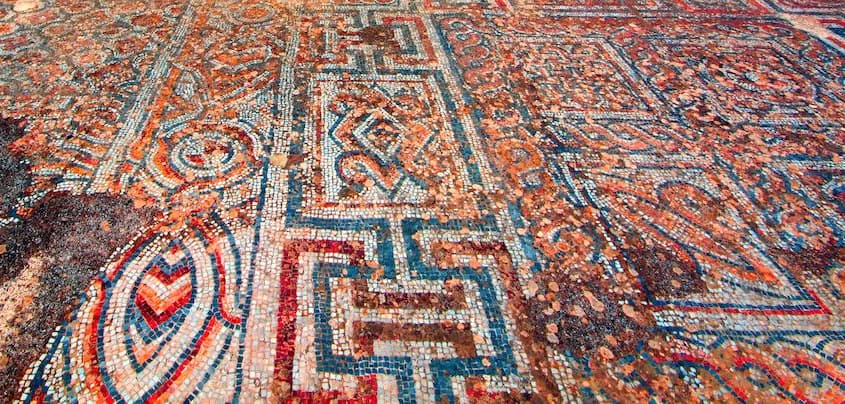 Mosaico geométrico de una acera de Éfeso, con grecas y rombos en rojo, azul y crema hechos de piedras pequeñas