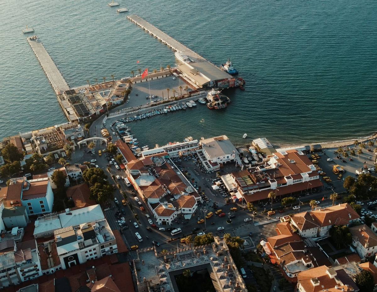 Vista aérea de los dos muelles del puerto de cruceros de Kuşadası, con los edificios de la terminal en su arranque, el puerto pesquero, los taxis de la salida y el patio del caravasar abajo