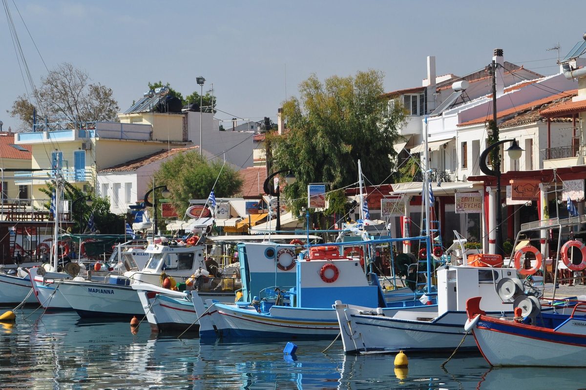 Barcas de pesca blancas y azules en el puerto de Pythagorio, en Samos, con terrazas y casas de tejado rojo en el paseo