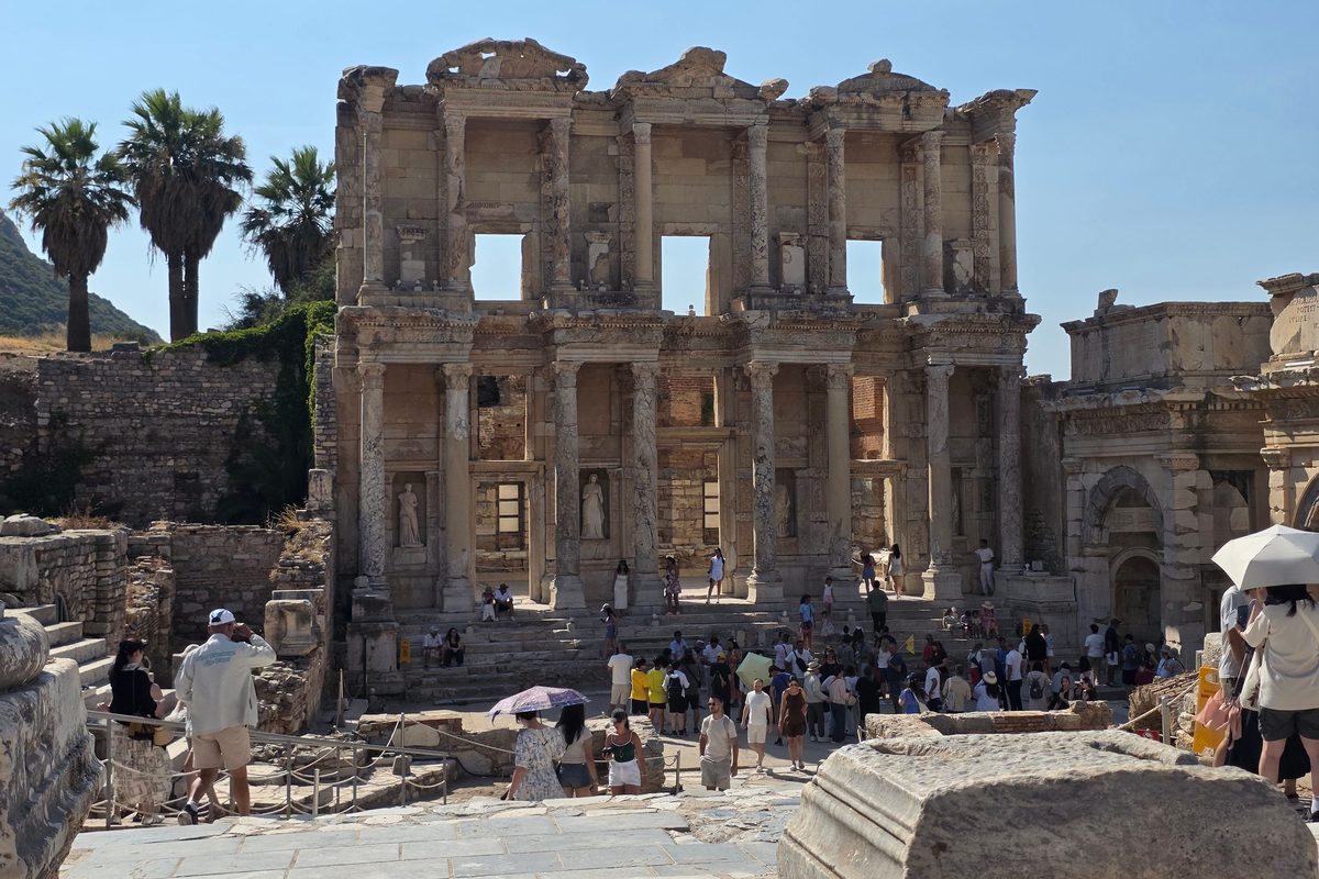 Visitantes en la plaza ante la Biblioteca de Celso de Éfeso un mediodía de verano, algunos con sombrillas contra el sol